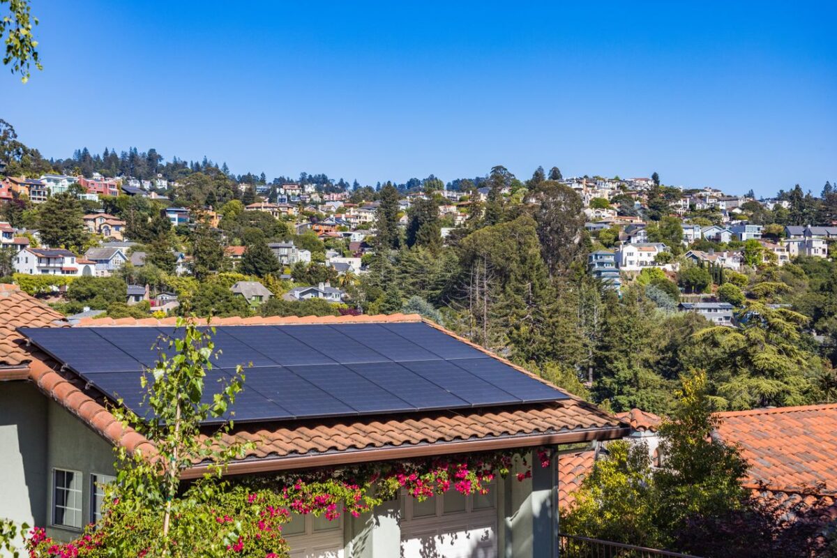 Offres Solar panels on a suburban home, surrounded by lush greenery and a sunny blue sky.