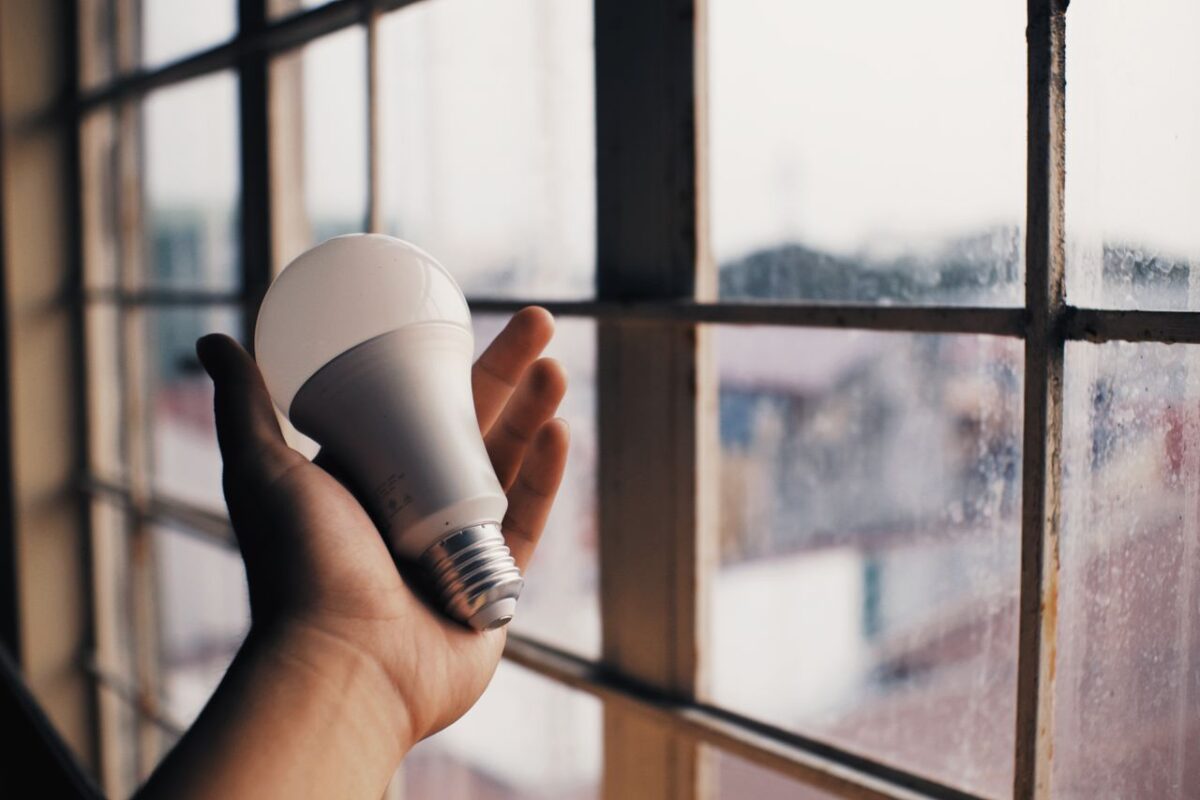 Offres Anonymous person holding energy efficient light bulb in hand on blurred background of big dusty window in light room