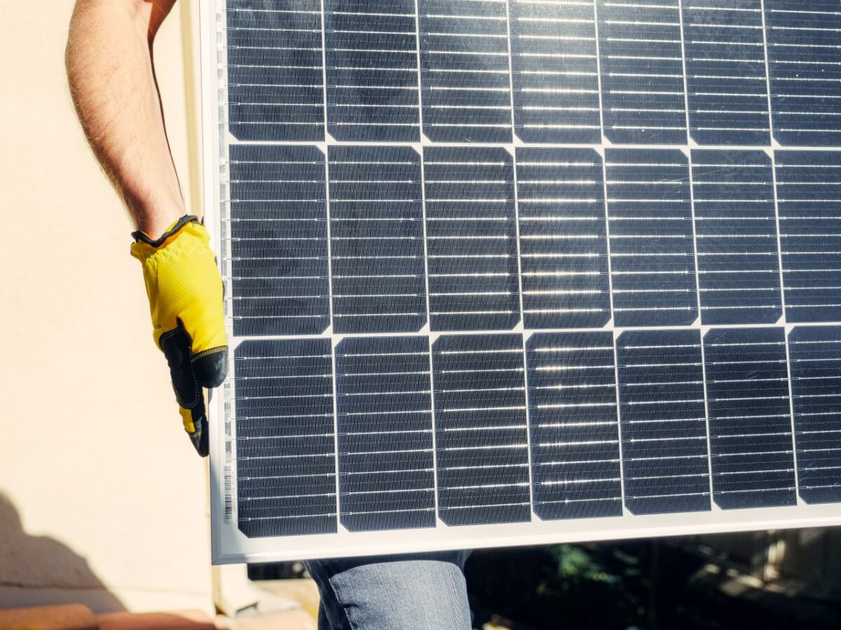 Offres Close-up of a person installing a solar panel outdoors under bright sunlight.